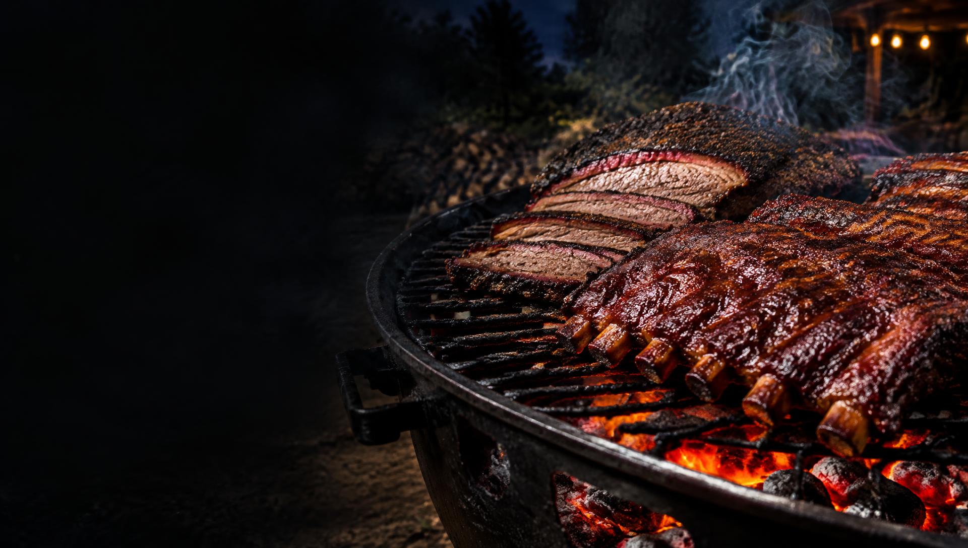 Smoked brisket and glazed ribs cooking over glowing charcoal